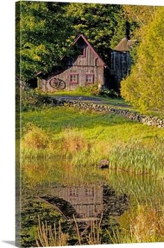 an old barn sits next to a pond in the middle of some grass and trees