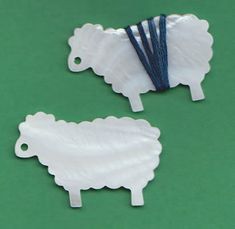 two white sheep shaped paper clips on a green surface with blue string attached to them