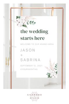 the wedding starts here sign with white flowers and greenery on it in front of a window