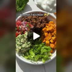 a white bowl filled with lettuce, carrots and other vegetables on top of a table