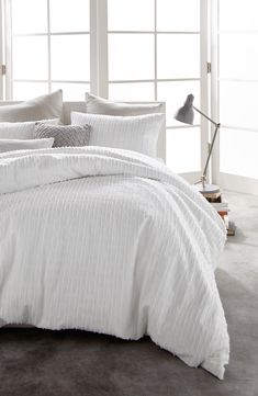 a bed with white comforter and pillows in a room next to a lamp on the floor