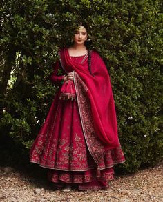 a woman standing in front of a bush wearing a red dress