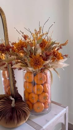 a vase filled with lots of oranges on top of a table next to a mirror