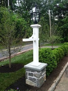 a large white cross sitting in the middle of a garden next to a sidewalk and trees