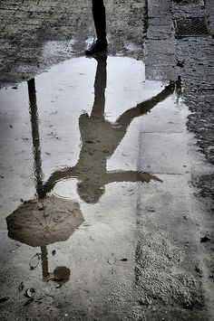 a person is standing in the rain with an umbrella reflected in it's puddle