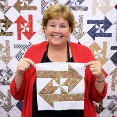 a woman holding up a piece of fabric in front of a quilted wall hanging