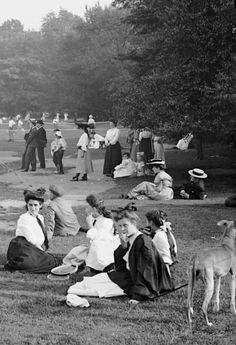 an old black and white photo of people sitting on the grass in front of trees