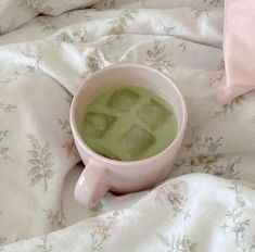 a cup filled with green liquid sitting on top of a bed