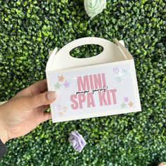 someone holding up a box with the words mini spa kit on it in front of a green wall