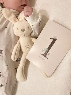 a baby laying in bed next to a book and a teddy bear with the number 1 on it