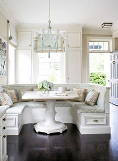 a kitchen with white cabinets and a table in the center, surrounded by built - in seating