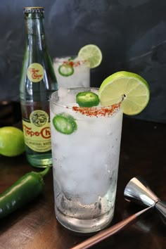 two glasses filled with ice and limes on top of a table next to bottles