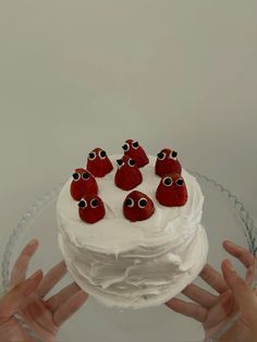 a cake with white frosting and red strawberries on top is being held by two hands