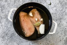 two pieces of chicken in a pot with onions and garlic on the side, top view