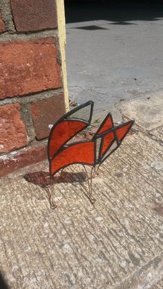 a red and black piece of art sitting on the ground next to a brick wall