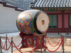 a large drum sitting on top of a wooden stand next to a red rope fence