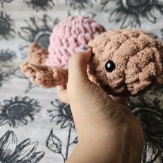 two small crocheted stuffed animals are being held by someone's hand on a bed