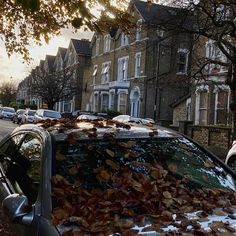 a car covered in leaves parked on the side of a road next to tall buildings