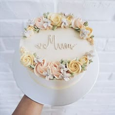 a white cake with yellow and pink flowers on it that says mom written in frosting