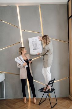 two women standing next to each other in front of a wall with papers on it