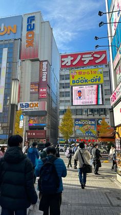 many people are walking down the street in front of tall buildings with advertisements on them