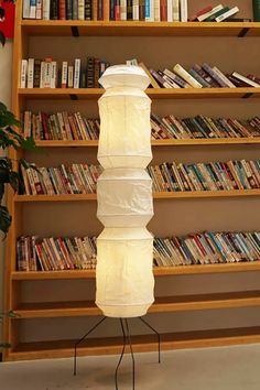 a tall lamp sitting on top of a metal stand in front of a bookshelf