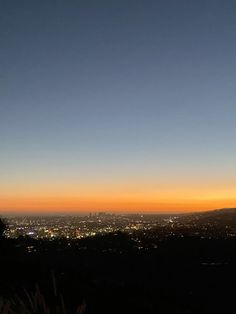 the sun is setting over a city and hills