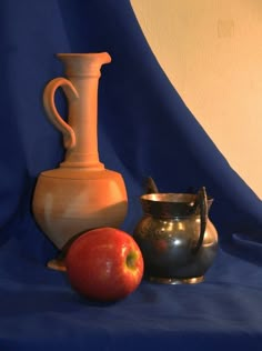 two vases and an apple sit on a blue table cloth next to each other