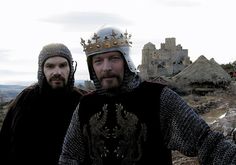 two men dressed in medieval clothing standing next to each other on top of a hill