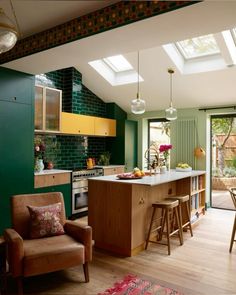 an open kitchen with green walls and wooden flooring, along with two chairs in front of the island