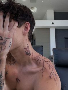 a shirtless man holding his hand to his face with tattoos on his chest and neck