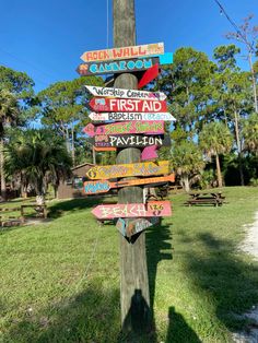 a wooden pole with many signs on it in the middle of a grassy area next to trees