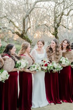 the bride and her bridesmaids are all dressed in red velvet dresses with fur stoles