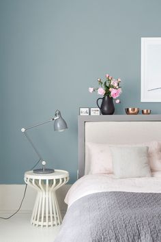 a bedroom with blue walls and pink flowers in the vase on the headboard next to the bed