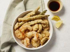 a white bowl filled with fried shrimp next to a cup of tea and lemon wedges