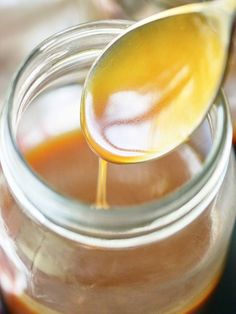 a spoon full of liquid is being poured into a glass jar with honey in it