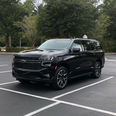 a black suv is parked in a parking lot with trees behind it and bushes on the other side