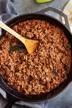 a skillet filled with ground beef and a wooden spoon in it next to an avocado