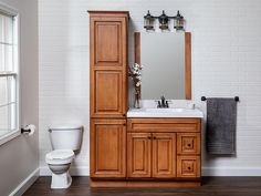 a white toilet sitting next to a wooden cabinet in a bathroom under a mirror and light fixture