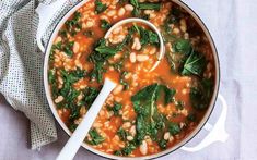 a pot filled with beans and spinach on top of a white cloth next to a spoon