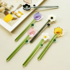 four different colored flower shaped hair pins on top of a white table next to a book