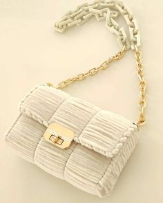 a white purse on a chain with a gold buckle hanging from it's shoulder