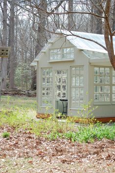 a small white house sitting in the middle of a forest with lots of leaves on the ground