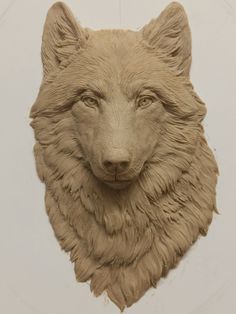 a clay sculpture of a wolf's head hanging on a wall in front of a white background