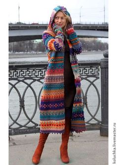 a woman standing next to a river wearing a colorful coat