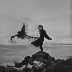 a woman standing on top of a rock next to an eagle flying over the ocean