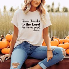 a woman sitting on top of a pile of pumpkins wearing a t - shirt that says give thanks to the lord for he is good