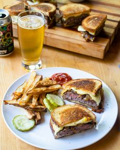 a white plate topped with a cut in half sandwich next to french fries and pickles