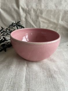 a pink bowl sitting on top of a white table cloth next to a black plant