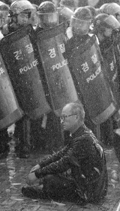 a man sitting on the ground in front of police officers with riot gear behind him